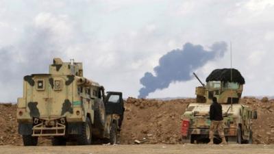 An Iraqi soldier looks on as smoke rises from oil wells in the Ajil field east of the city of Tikrit in the Salahuddin provinc