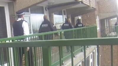 Back view of members of National Crime Agency approaching a flat as part of a raid against cybercrime suspects