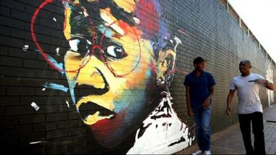 Graffiti on a wall as DJ edu walks past with an entrepreneur