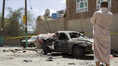 Man stands by vehicle destroyed in suicide attack