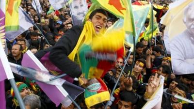 People gesture while others wave Kurdish flags