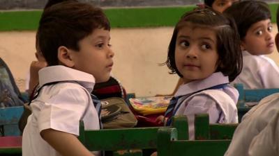 Indian schoolchildren turning round as they sit at desks in a Delhi classroom