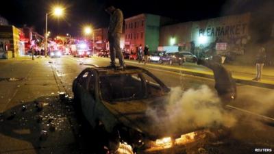 A rioter stands atop a burning car
