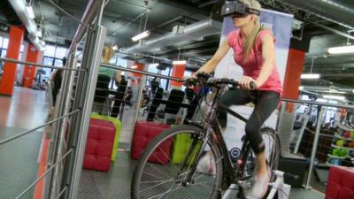 BBC Click's Lara Lewington rides a bicycle wearing a virtual reality headset