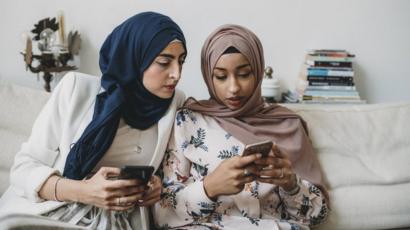 امرأتان عربيتان تنظران في هاتفيهما المحمولين
