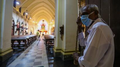 A Sri Lankan man wearing a protective mask ring the church bells for the start of Easter Sunday service at the almost deserted all Saints church during an island-wide curfew, in Colombo, Sri Lanka