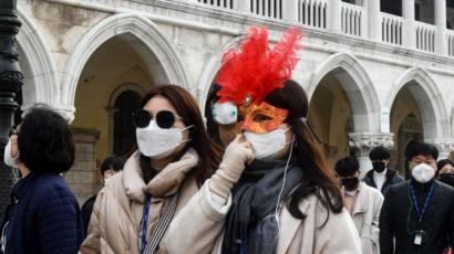 Tourists wearing protective facemasks and a Carnival mask visit the Piazza San Marco, in Venice