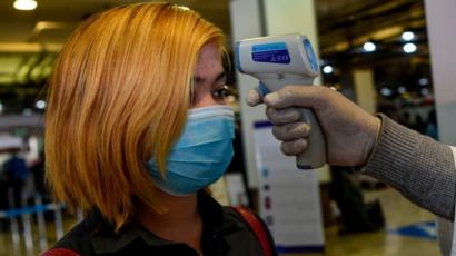 Una mujer es examinada con un termómetro en un aeropuerto.