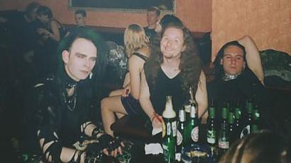Three goths and a table crowded with beer bottles, in a nightclub