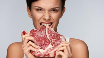 Mujer mordiendo un pedazo de carne roja cruda.