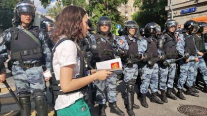أولغا تمشي أمام أفراد الشرطة وبيدها نسخة من الدستور الروسي