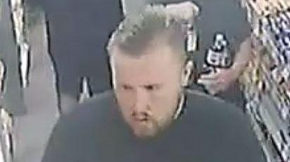 A man with gelled back hair, with a goatee beard, in what looks like a supermarket or small shop