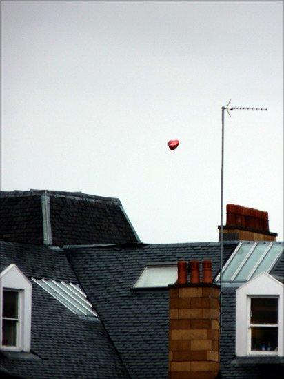 Heart-shaped balloon floating over rooftops