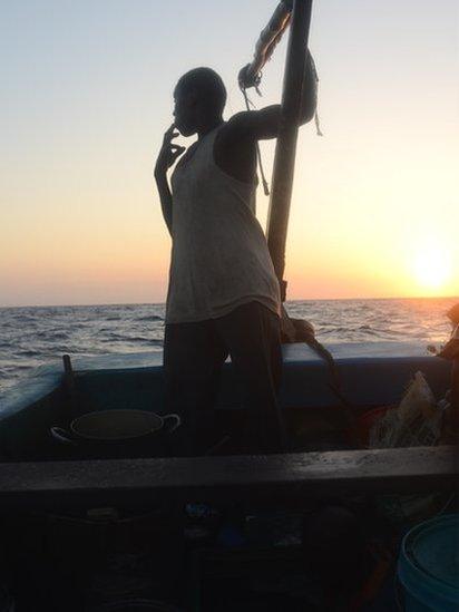 A crewman aboard the Kenyan fishing vessel looks out to sea smoking a cigarette as the sun sets