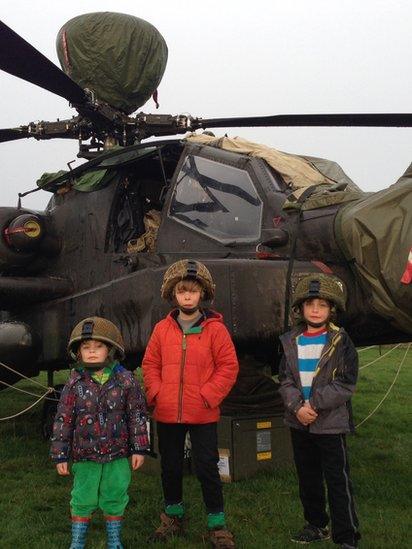 Children standing in front of an Apache helicopter