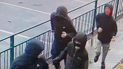A grainy image of four youths wearing face masks and dark jackets with their hoods up