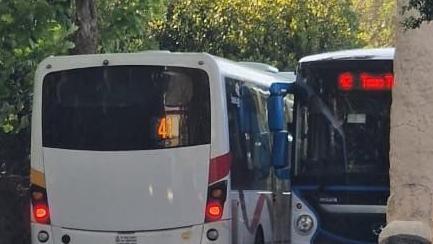 A white bus colliding with a blue bus in a tight space