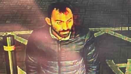 CCTV image of the man police want to speak to. He has dark hair and facial hair and is wearing a dark coat. 