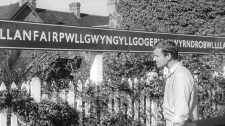 A reporter looks at a sign for Llanfairpwllgwyngyllgogerychwyrndrobwllllantysiliogogogoch.