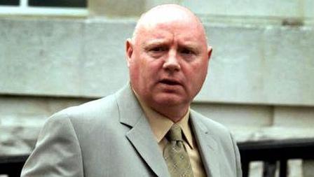 William Stobie, a bald man wearing a grey suit, yellow shirt and yellow tie looks towards the camera