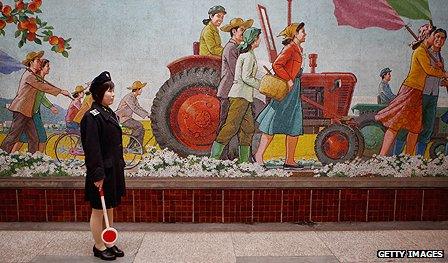 Official stands beside a mural in a Pyongyang metro