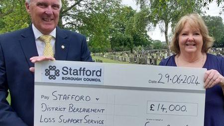 A man and a woman hold up a large replica cheque