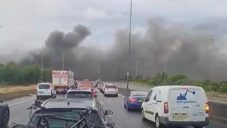 A blurry photo of a busy motorway with thick black smoke billowing across both carriageways in the distance