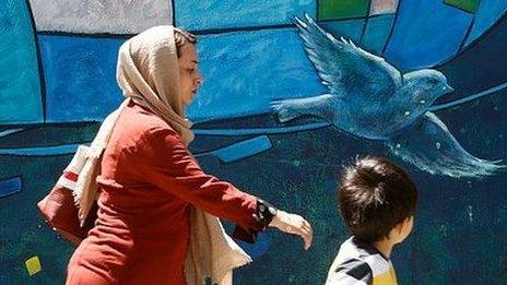 woman and child walk past mural with birds in Iran