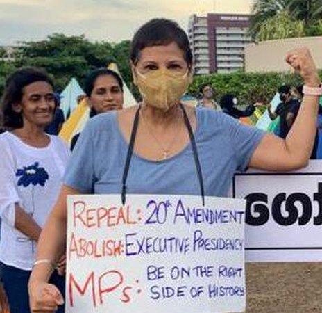 Женщина протестует, носит табличку и показывает символ силы