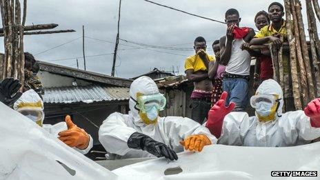 Workers in protective suits discard of body bag