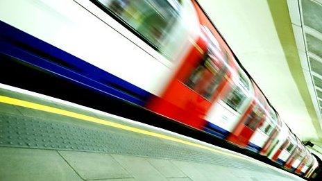 A Tube train moving quickly past a platform.