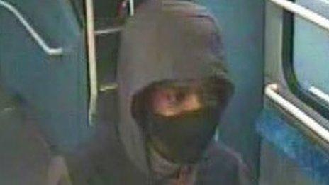 Image of the man wearing a black and grey hooded coat with a red zip and a black facemask.