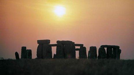 Stonehenge in silhouette in front of a hazy sun