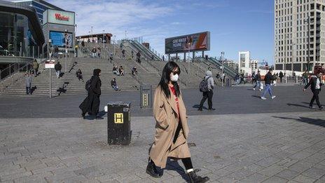 A few shoppers walk beneath blue skies as lockdown begins.