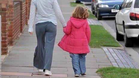 Library shot of parent leading a girl with a pink coat along a pavement
