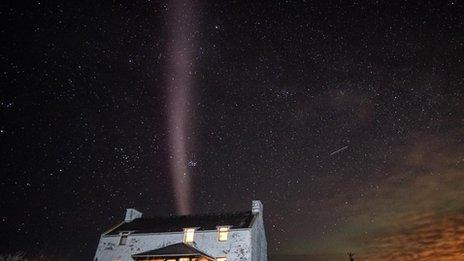 Pale purple ribbon of light in night sky above a house