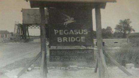 A black and white image of a "Pegasus Bridge" sign on the bridge