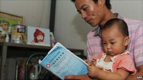 Chinese man Wang Gang holds his daughter Xiaoying, 13 months, at their home in Beijing on 10 August as he reads a doctor's report on his daughter's diagnosis of premature breast growth