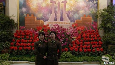 North Korean female soldiers pose for photographs in front of a display of 'kimjongilia' and 'kimilsungia' flowers