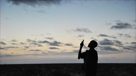A militiaman looks into his mobile phone as he searches for a network signal in the early morning hours while travelling through the plains of central Somalia on 21 August 2010