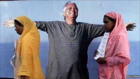 Grameen Bank employees walk in front of a portrait of Muhammad Yunus