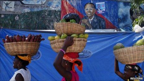 Women walk past a mural of former president Jean-Betrand Aristide in Port-au-Prince