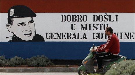 A resident rides on a scooter past a mural depicting Gen. Ante Gotovina inside Croatian national colours, with text reading: "Welcome to Gen. Gotovina"s place" in Pakostane, southern Croatia, Thursday, April 14
