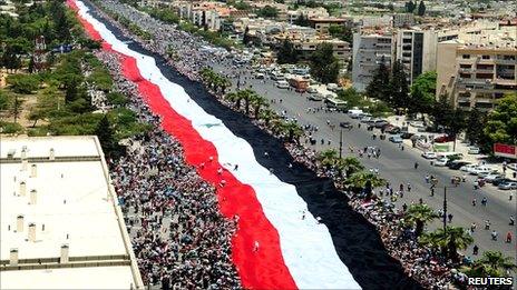Pro-government protesters carry a large Syrian flag along the al-Mezzeh highway in Damascus on 15 June 2011
