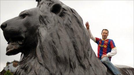 A football fan sits on a lion statue in Trafalgar Square