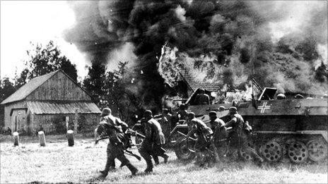 German soldiers, backed by armoured personnel carriers, move into a burning village somewhere along the German-Soviet front, 26 June 1941