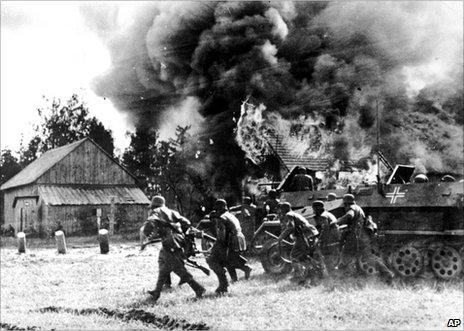 German soldiers, backed by armoured personnel carriers, move into a burning village somewhere along the German-Soviet front, 26 June 1941