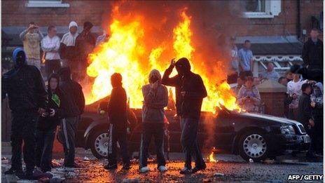 Masked youths in front of burning car