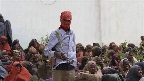 An Al Shabaab soldier stands next to women during food distribution at a displaced persons camp in Shebelle, about 50 km (31 miles) south of the capital Mogadishu, July 6, 2011