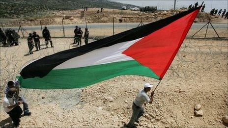 A Palestinian man holds the flag as Israeli border police officers look on in Bilin, near Ramallah, 2006
